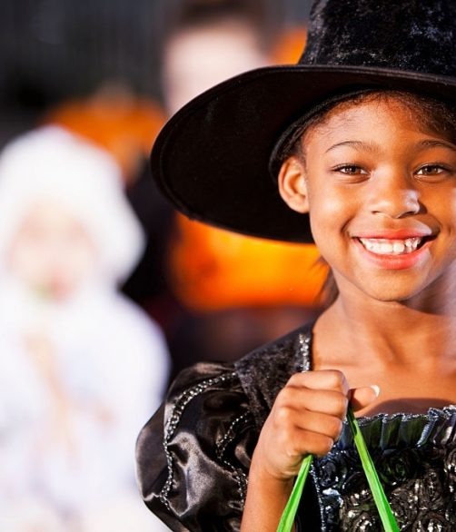 African American girl (7 years) dressed up as witch for halloween, eating candy.