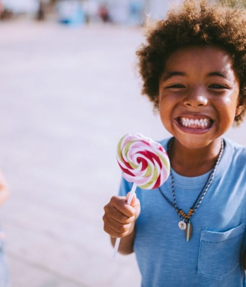 Happy multi-ethnic mixed family little boys eating lollipops in summer in the city