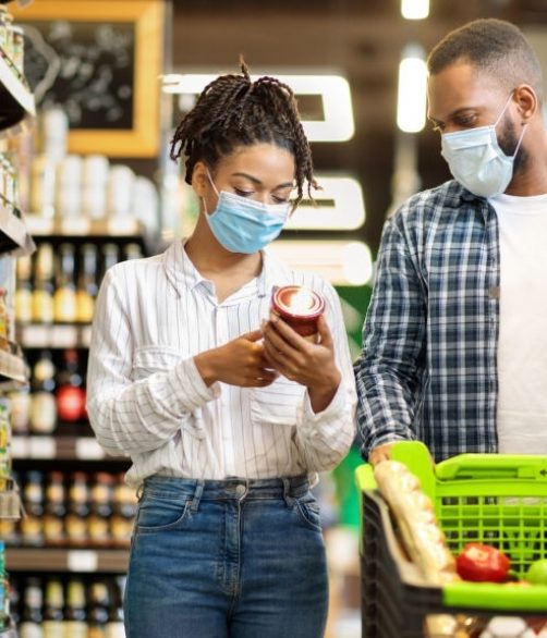 African Family Couple In Shop Buying Groceries Wearing Face Mask Choosing Food Goods Walking With Shopping Cart In Supermarket Store. Customers Buy Essentials During Pandemic. Panorama, Free Space