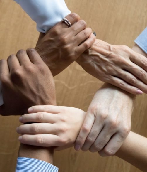 Diverse business people team connected grasping hands holding each other wrists in circle, loyalty help in teamwork concept, professional trust power support unity solidarity, close up top view above