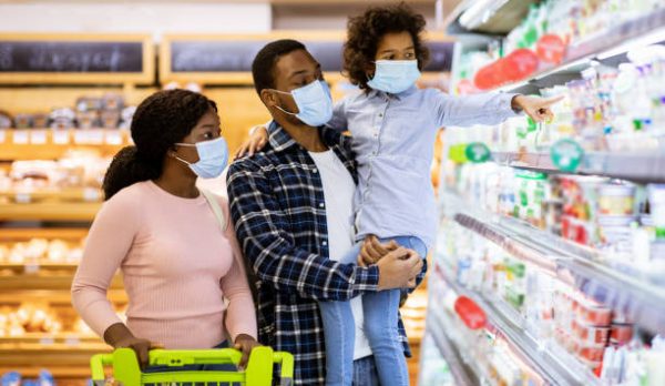 Family shopping during coronavirus pandemic. African American family with child wearing face masks, purchasing food at supermarket, panorama. Black parents with their kid buying products at mall